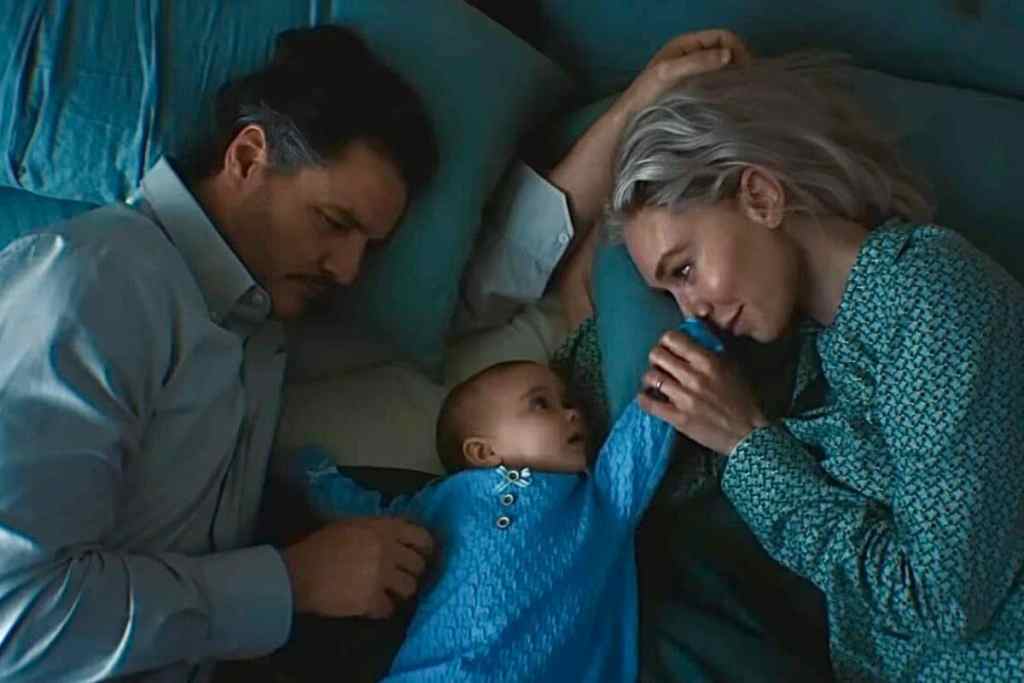 A family of three, with a man and woman lying on a bed, gently interacting with their infant child. The scene conveys warmth and intimacy, with soft blue bedding and a calm atmosphere.