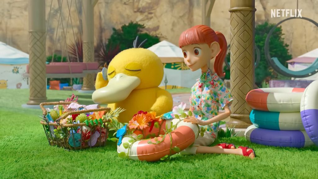 A scene from the stop-motion series Pokémon Concierge featuring a girl sitting on the grass next to a Psyduck, with a basket of flowers and colorful floating rings nearby.