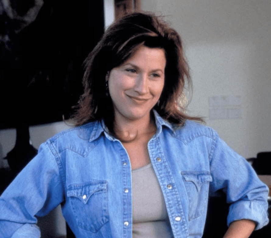 A woman with shoulder-length brown hair smiles warmly while wearing a denim shirt over a light top.